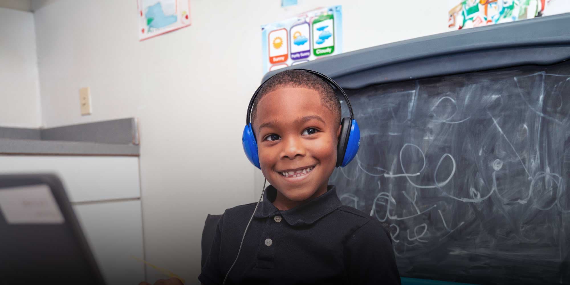Smiling student wearing blue headphones in a classroom.