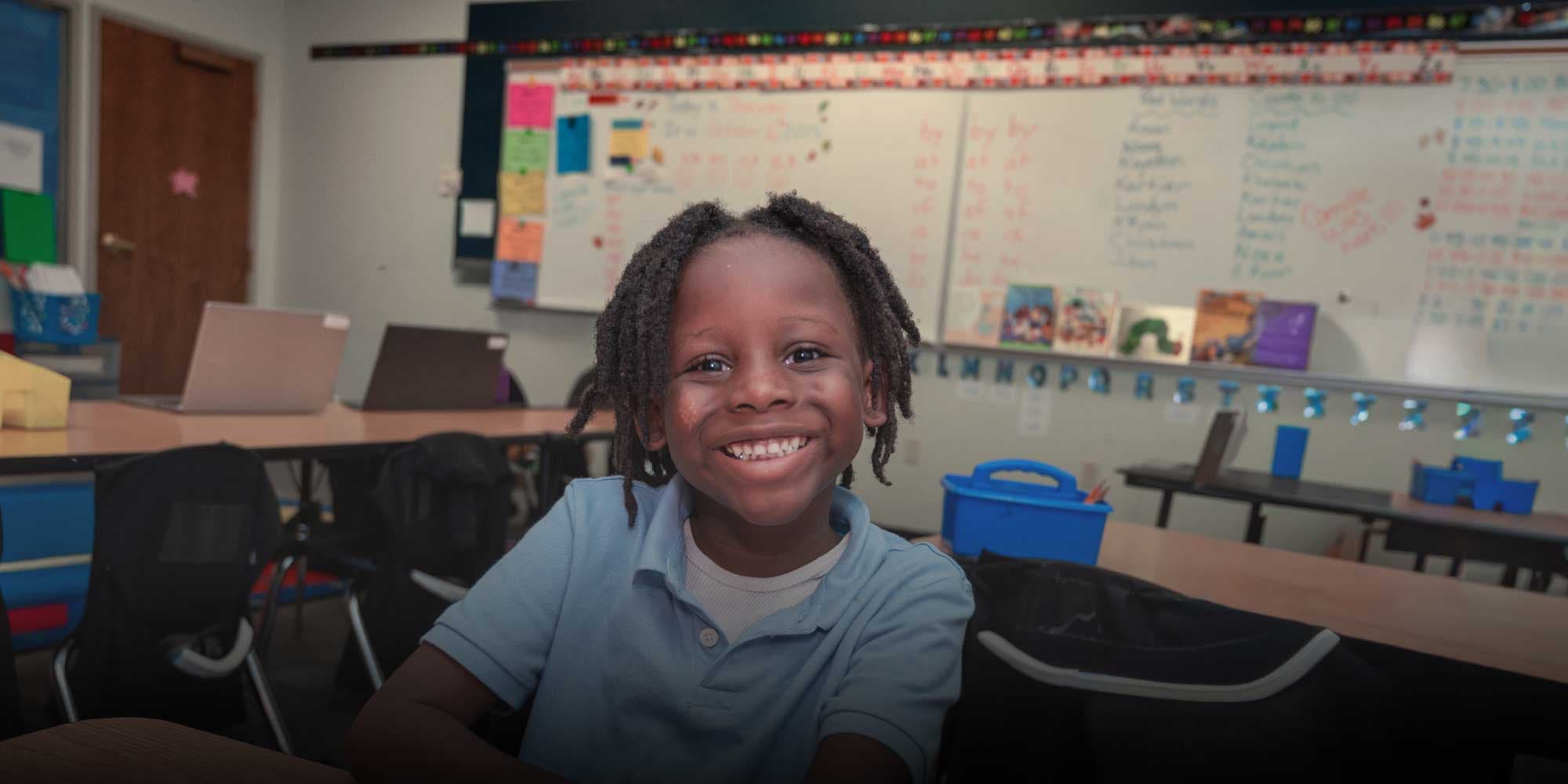 Smiling student seated at a classroom desk.